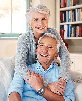 Senior woman hugging senior man on couch from behind